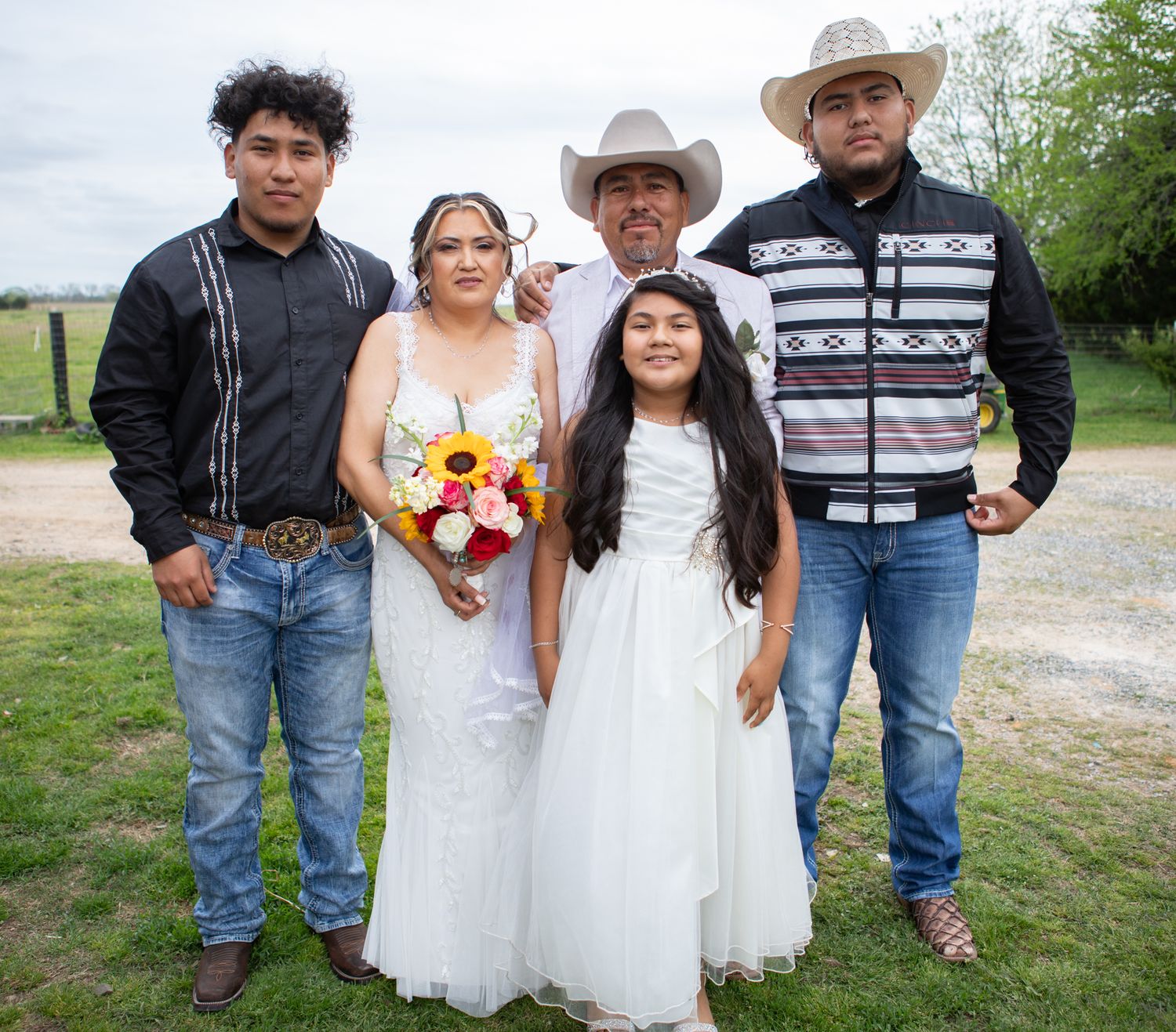 Family group poses outdoors wearing western attire and cowboy hats for a casual wedding photo.