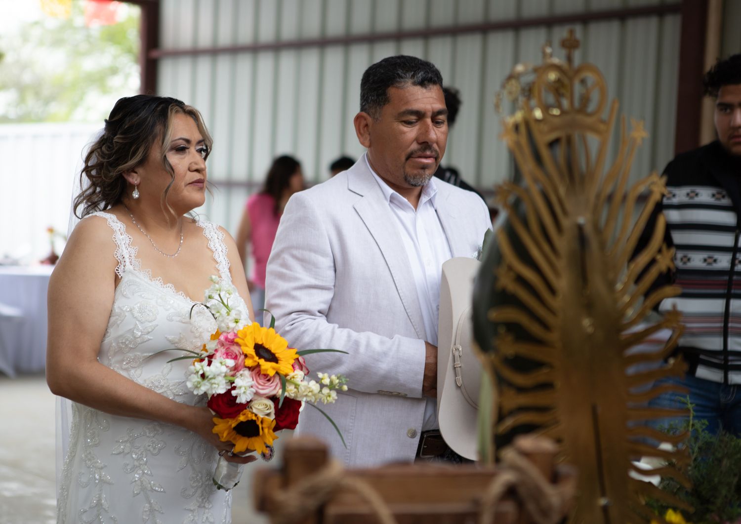 A couple participates in a wedding ceremony in front of a decorative golden backdrop.