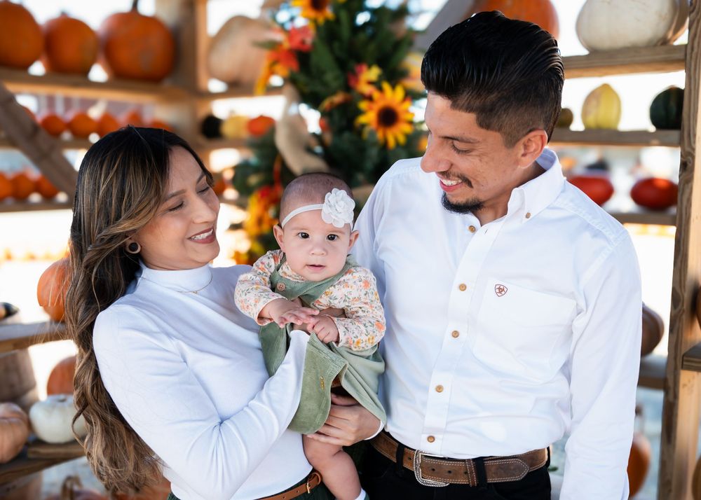 Happy young family with baby poses at pumpkin patch during fall family photo session.