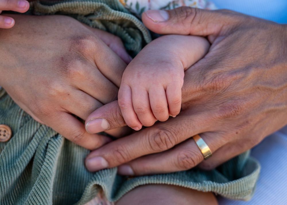 Close-up of baby hands held by parents wearing wedding ring during family photo session.