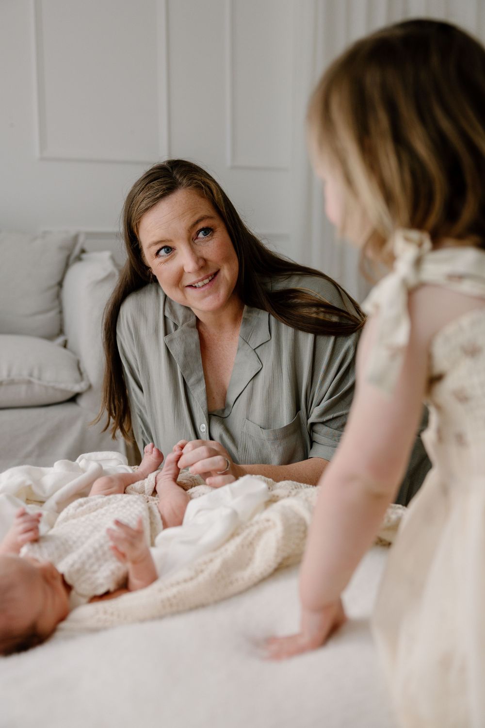 Candid family moment on white couch with newborn baby and children.
