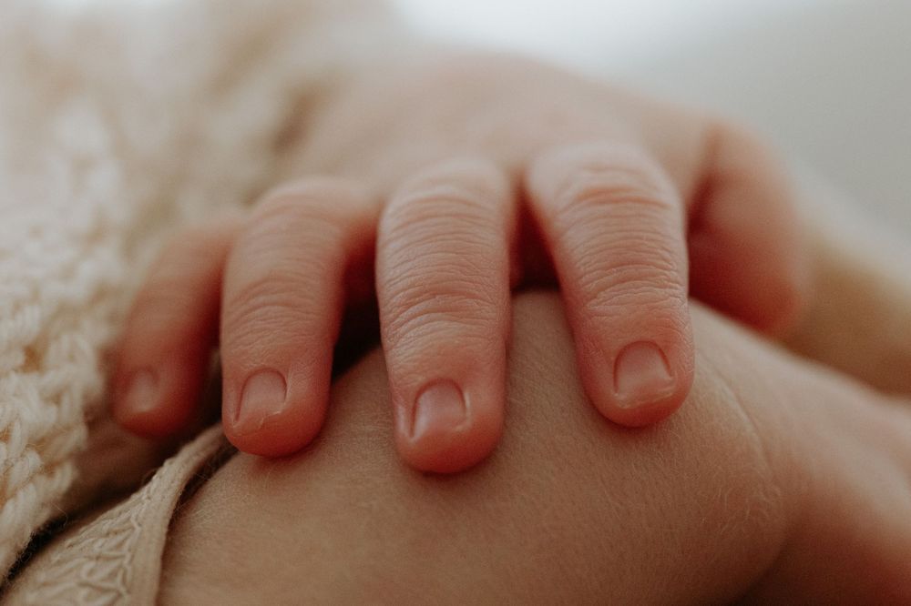Close-up of tiny baby fingers resting on soft knitted fabric.