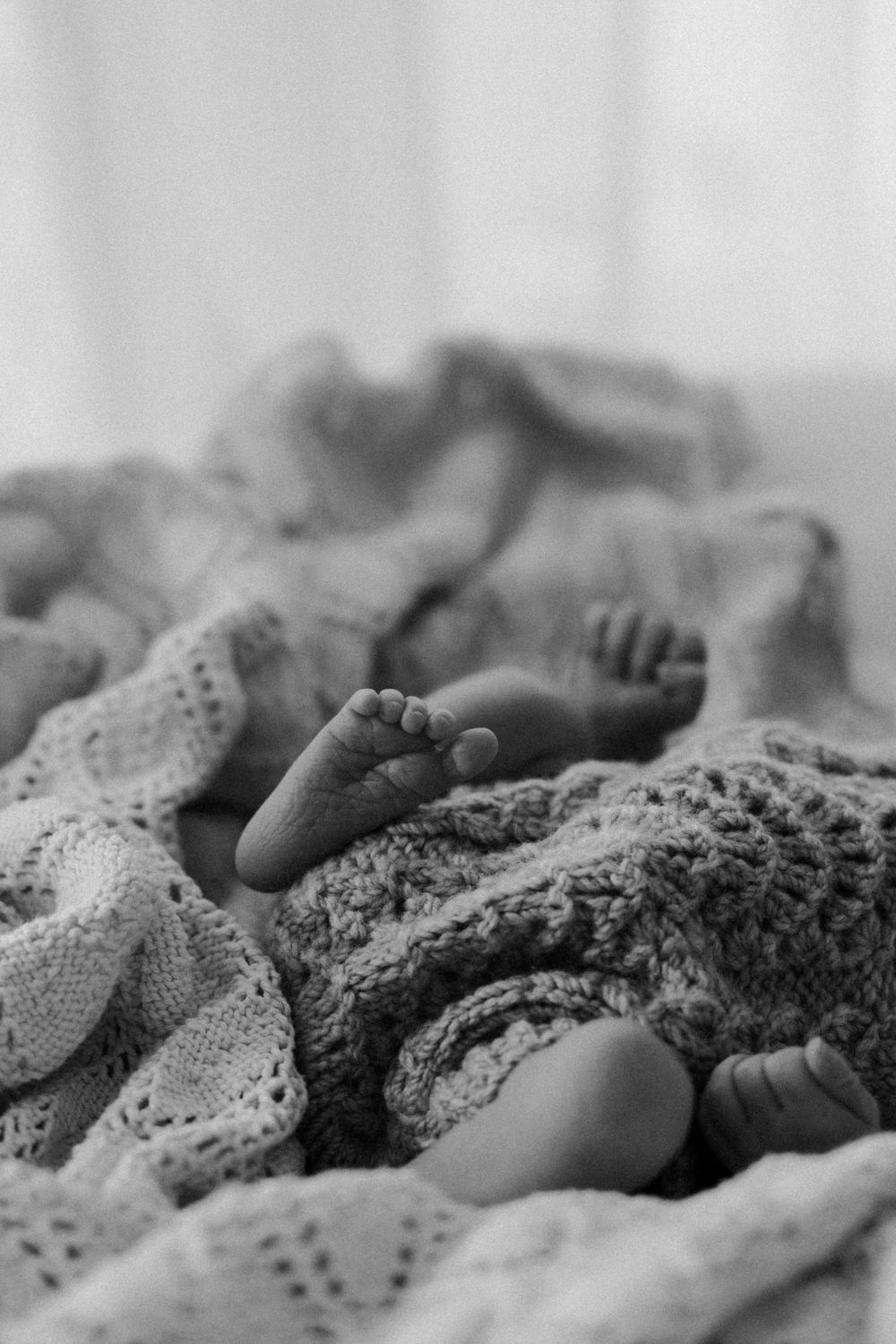 Black and white image of tiny baby feet wrapped in delicate knit blanket.