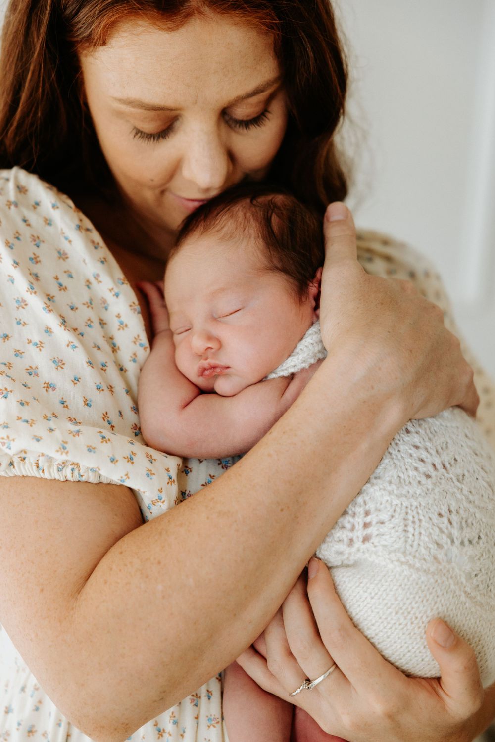 Tender moment of mother holding sleeping newborn swaddled in white.