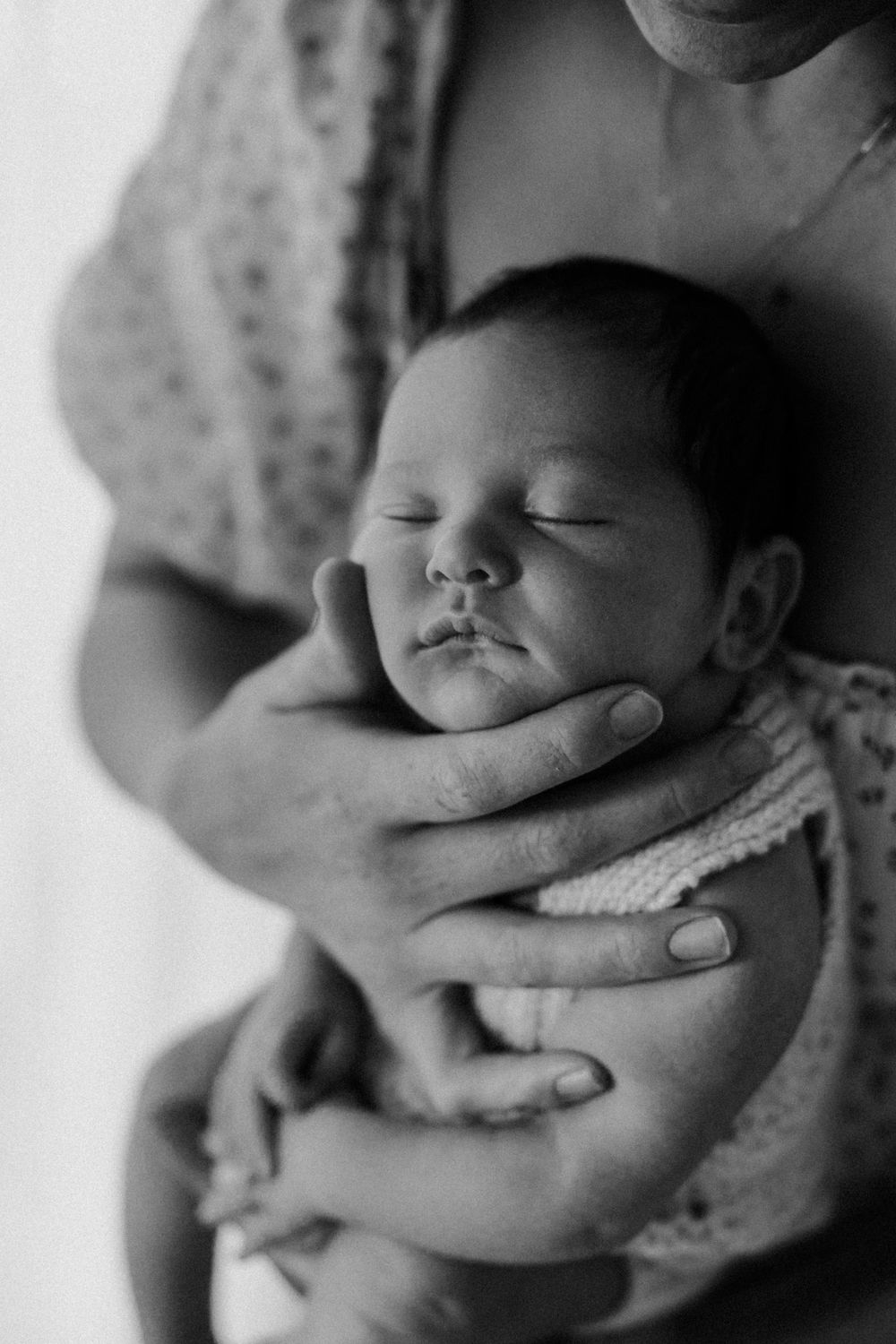 Black and white portrait of sleeping newborn being cradled gently.