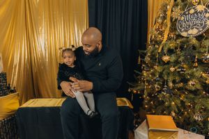 A couple embraces in front of a decorated Christmas tree with golden curtains in the background.