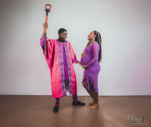 Two dancers in vibrant pink and purple costumes perform expressive movements in a minimalist studio setting.