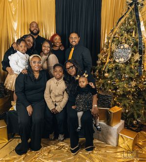 Family group poses together in formal attire by decorated Christmas tree in elegant gold and green setting.