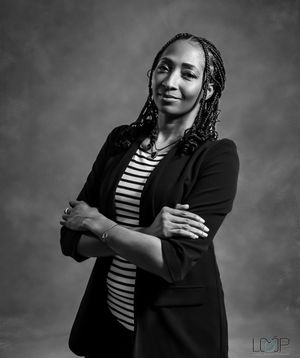 A person in a striped shirt and black blazer poses expressively in a black and white portrait series.
