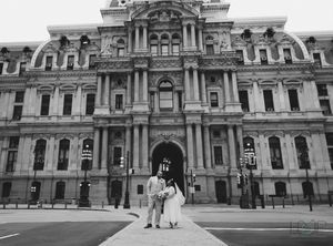 A black and white photo of two people walking in front of the ornate facade of Philadelphia City Hall.