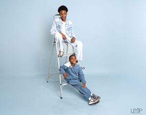 Two people posing on a stepladder in matching light denim outfits against a blue background.