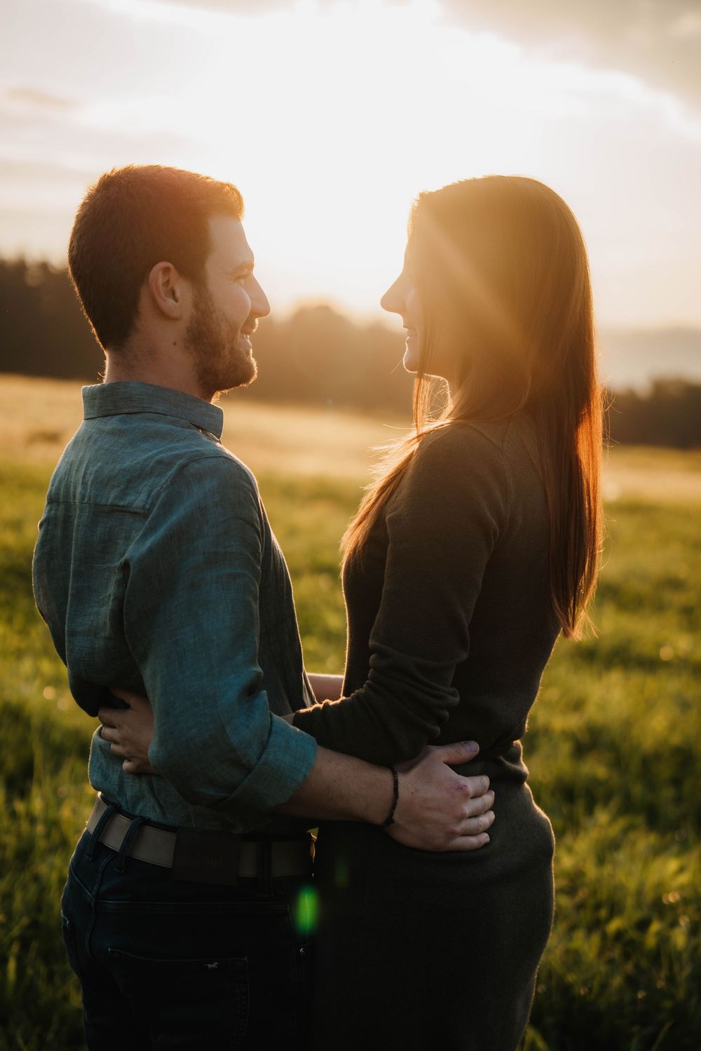 A couple embraces in a sunlit field during golden hour creating a romantic silhouette against the setting sun.