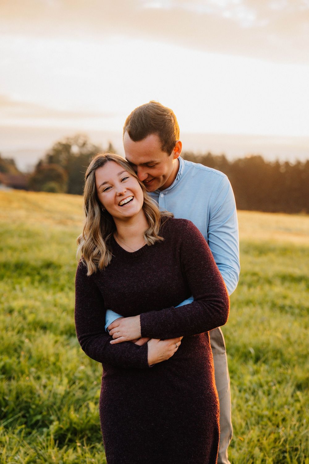 Couple sharing joyful laughter together in a sunlit meadow during golden hour.