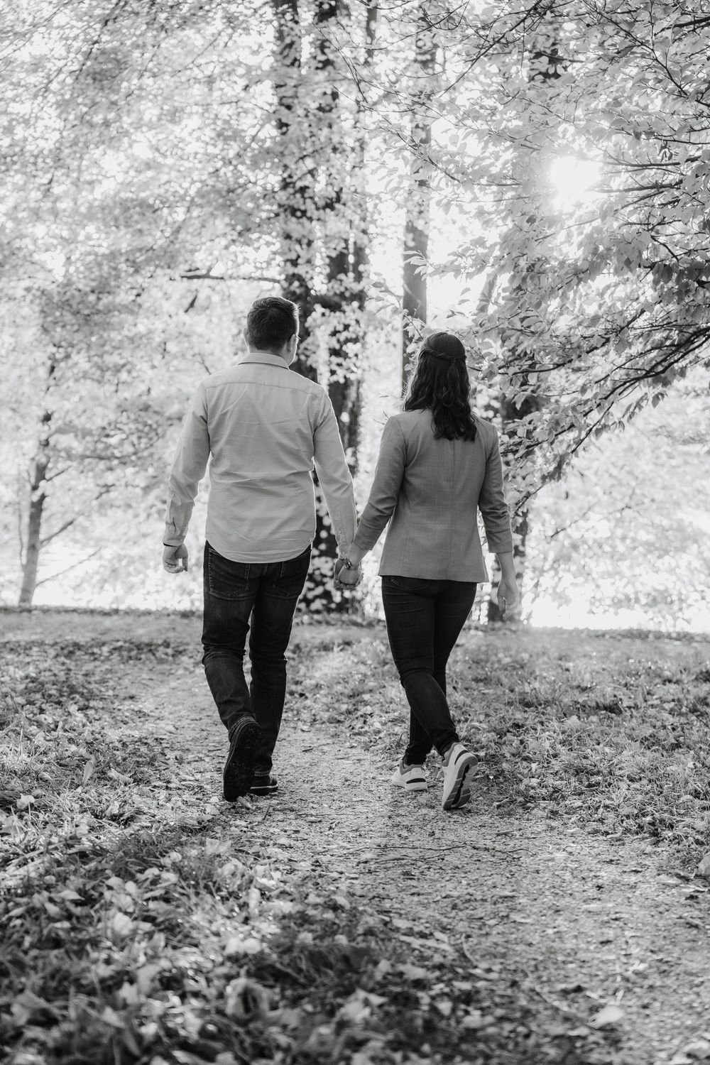 A couple walks together through a serene wooded path in black and white.