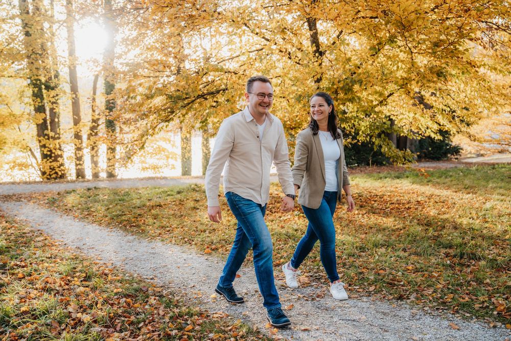 Couple walking hand in hand on an autumn path surrounded by golden trees.