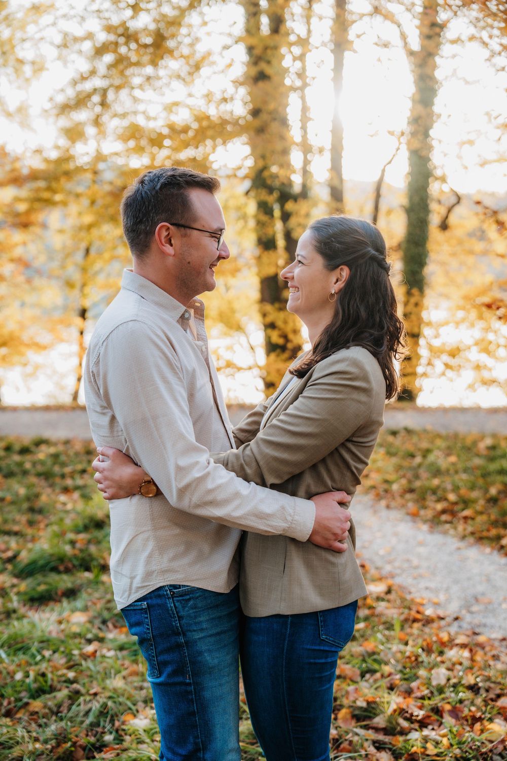 Couple embracing and laughing together among fall foliage on a woodland path.