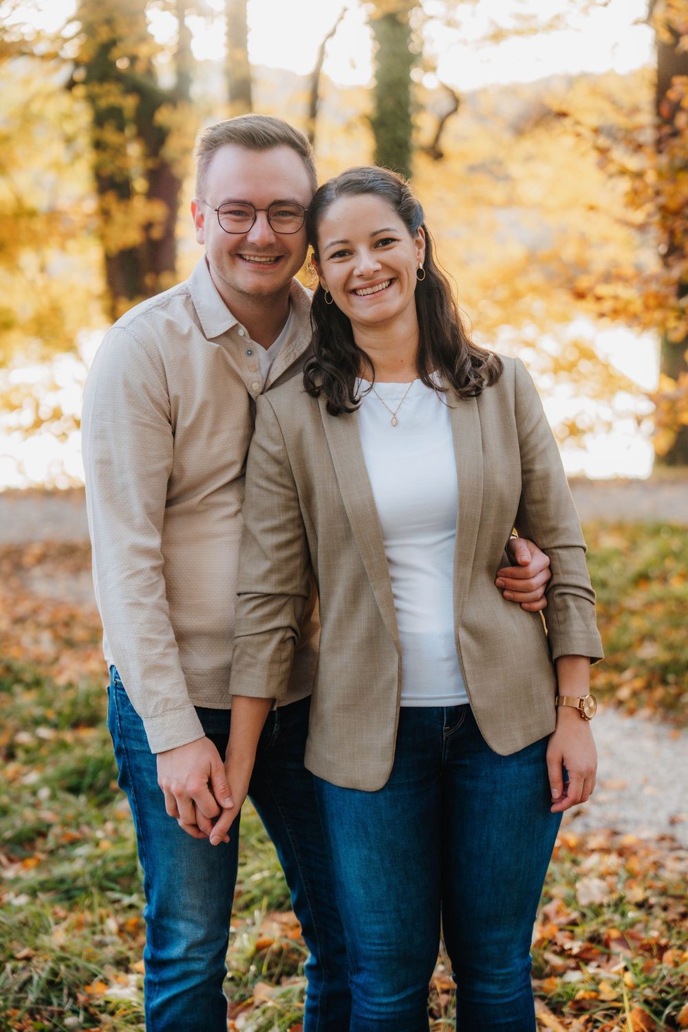 A couple shares a playful moment while posing for photos in a fall setting with golden leaves.