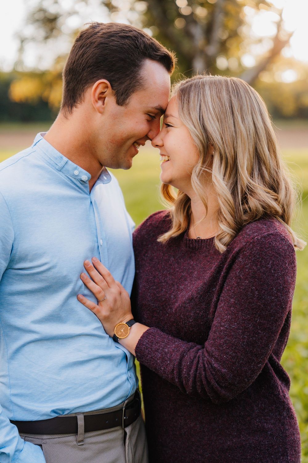 Romantic couple in blue and burgundy sweaters share intimate moments in a golden hour outdoor setting.