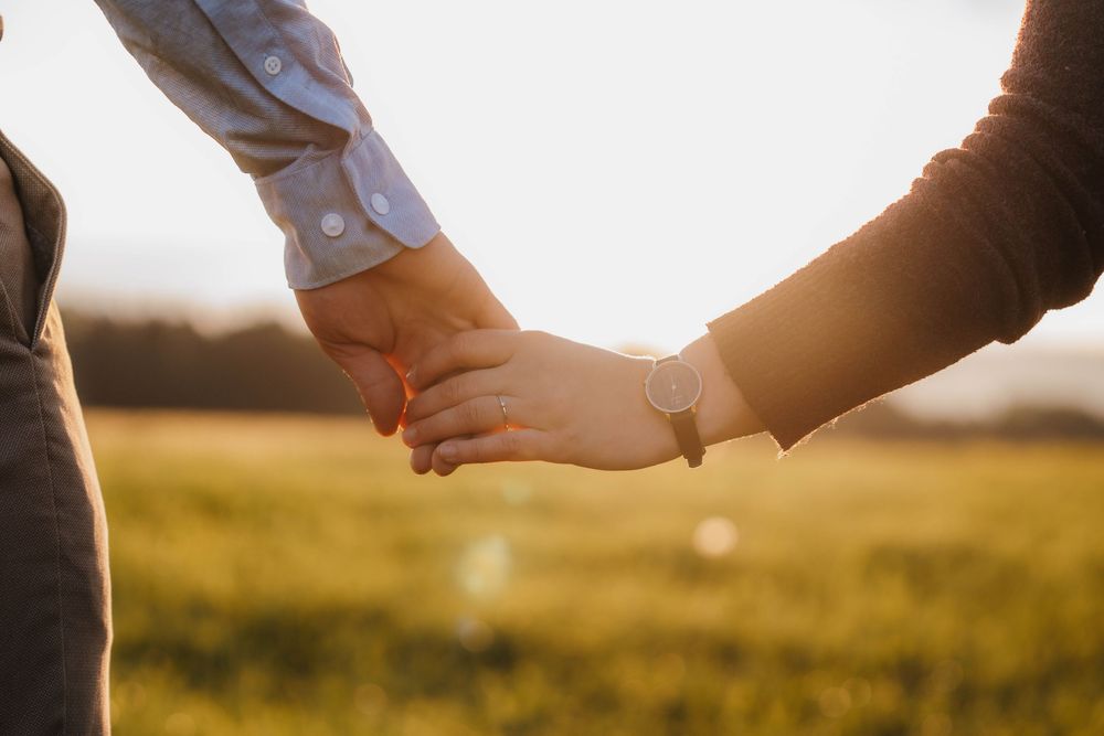 Hands lovingly intertwined against golden sunset light in an outdoor setting.