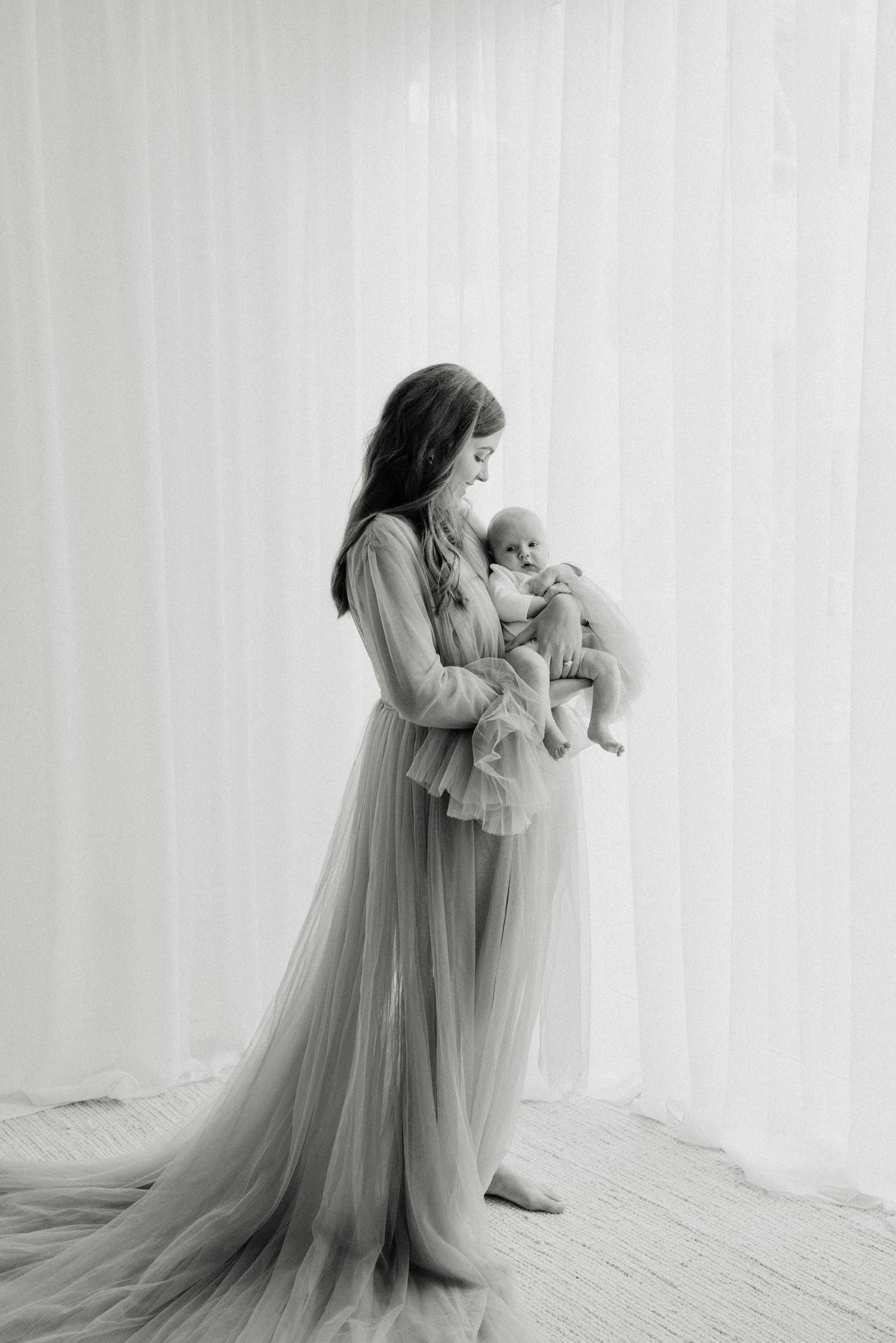 A tender black and white portrait of figure in flowing tulle gown holding a small infant.