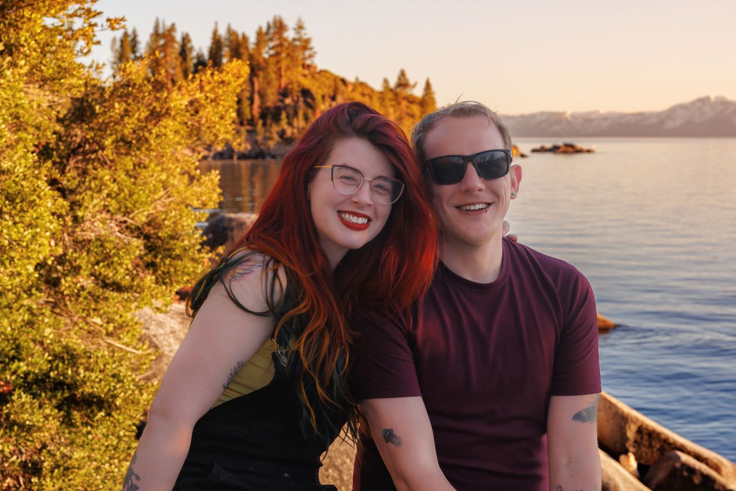 Couple enjoying a scenic sunset by the water with autumn trees in the background.