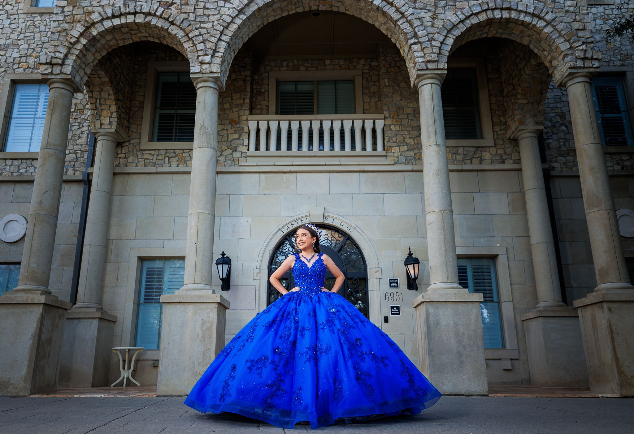 Quinceañera in a royal blue gown in front of an arched stone entrance