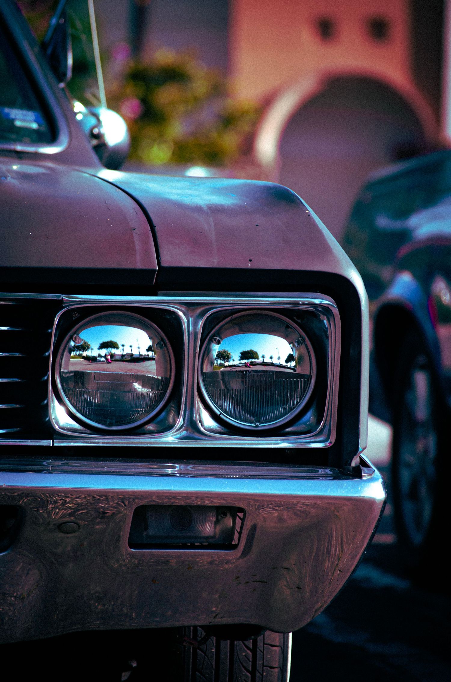 Close-up of vintage car headlights reflecting a scenic view at dusk.