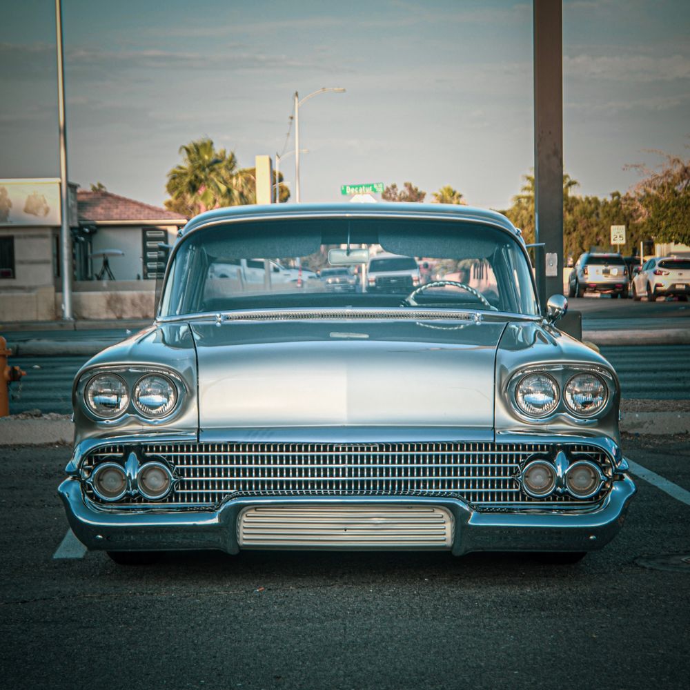 Classic light blue 1958 Chevrolet with chrome grille parked in urban setting at dusk.