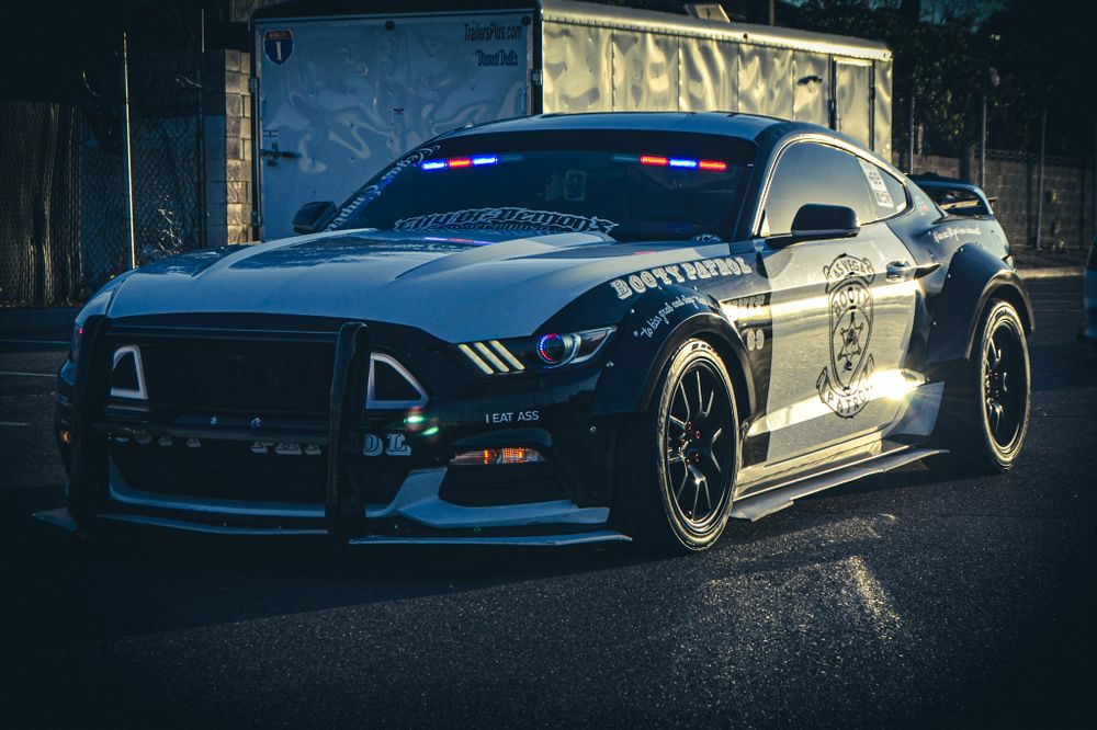 Black Ford Mustang police vehicle with custom modifications parked in dark setting.