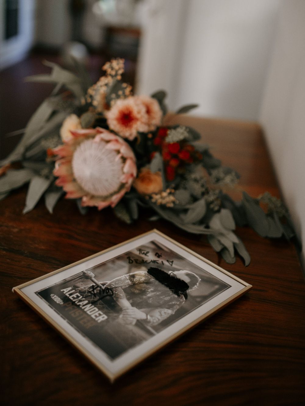 Wedding bouquet with protea and eucalyptus beside a framed black and white photo on wooden table.