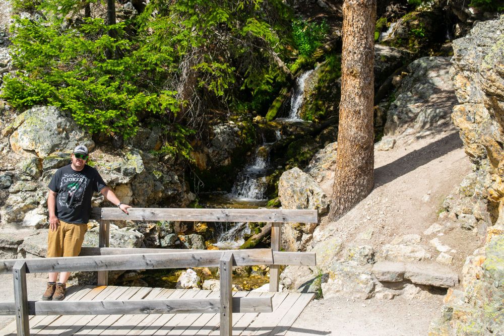 Wooden viewing platform overlooking cascading waterfall in rocky forest terrain.