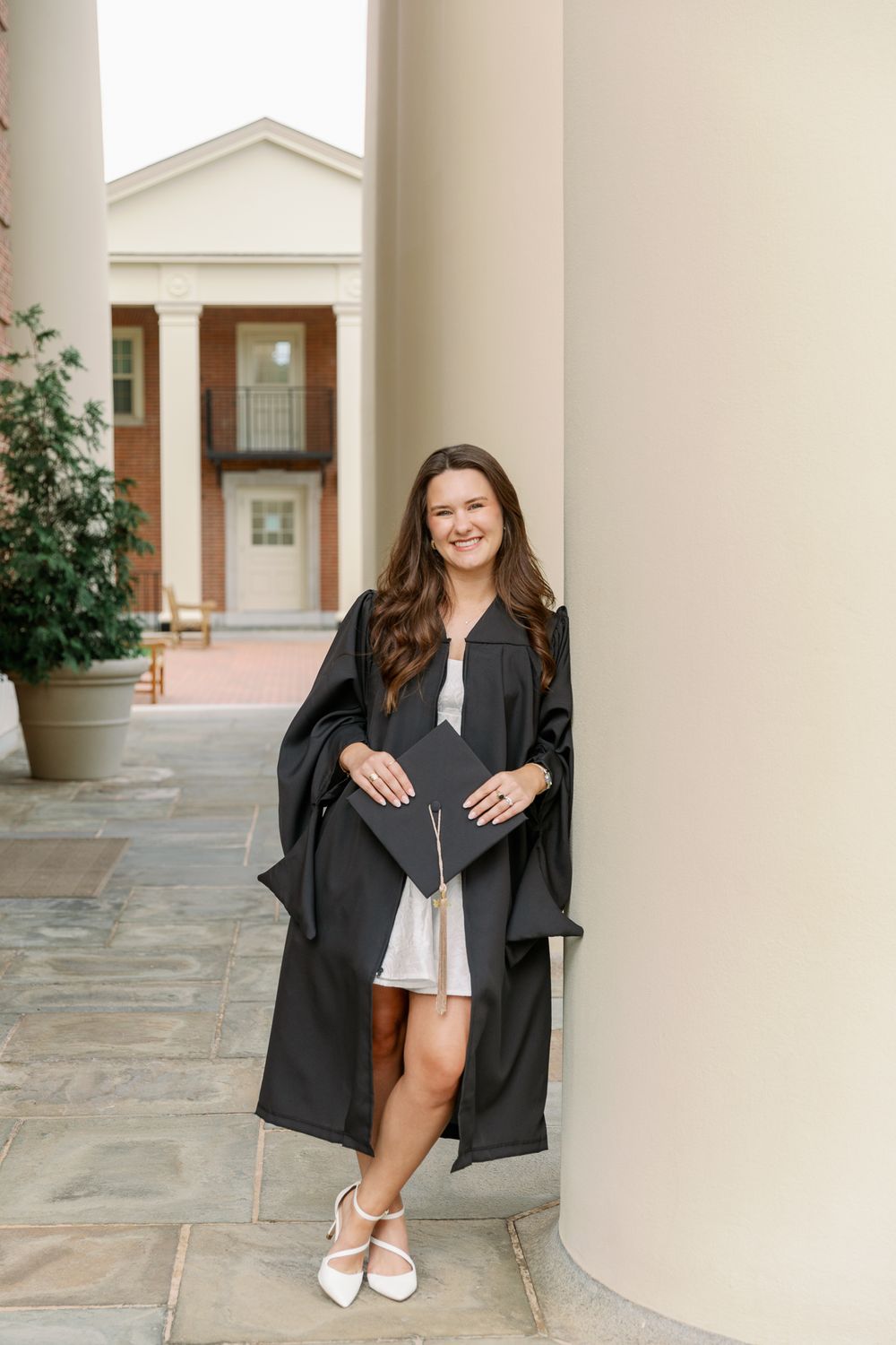 Graduate in academic dress stands between columns holding diploma.