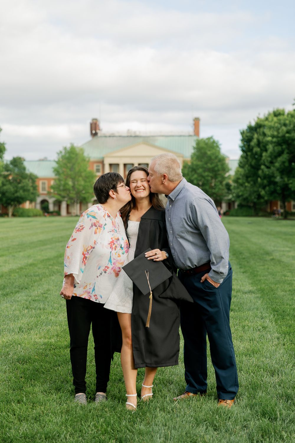 Family members share emotional embraces on a grassy lawn during graduation celebrations.