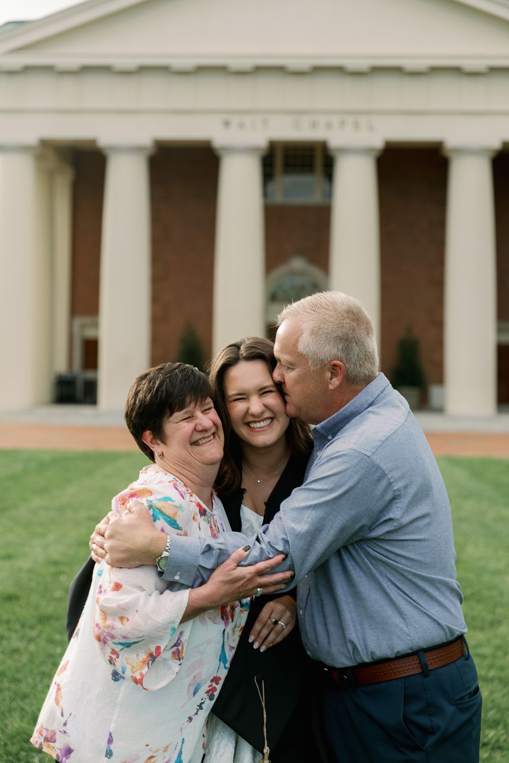 Joyful family moment on lawn in front of brick chapel building.