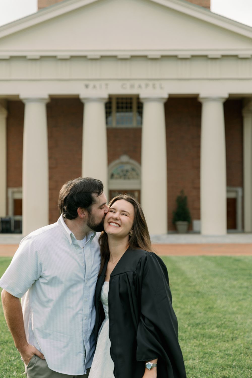 Couple shares tender moment on lawn with Wait Chapel in background.