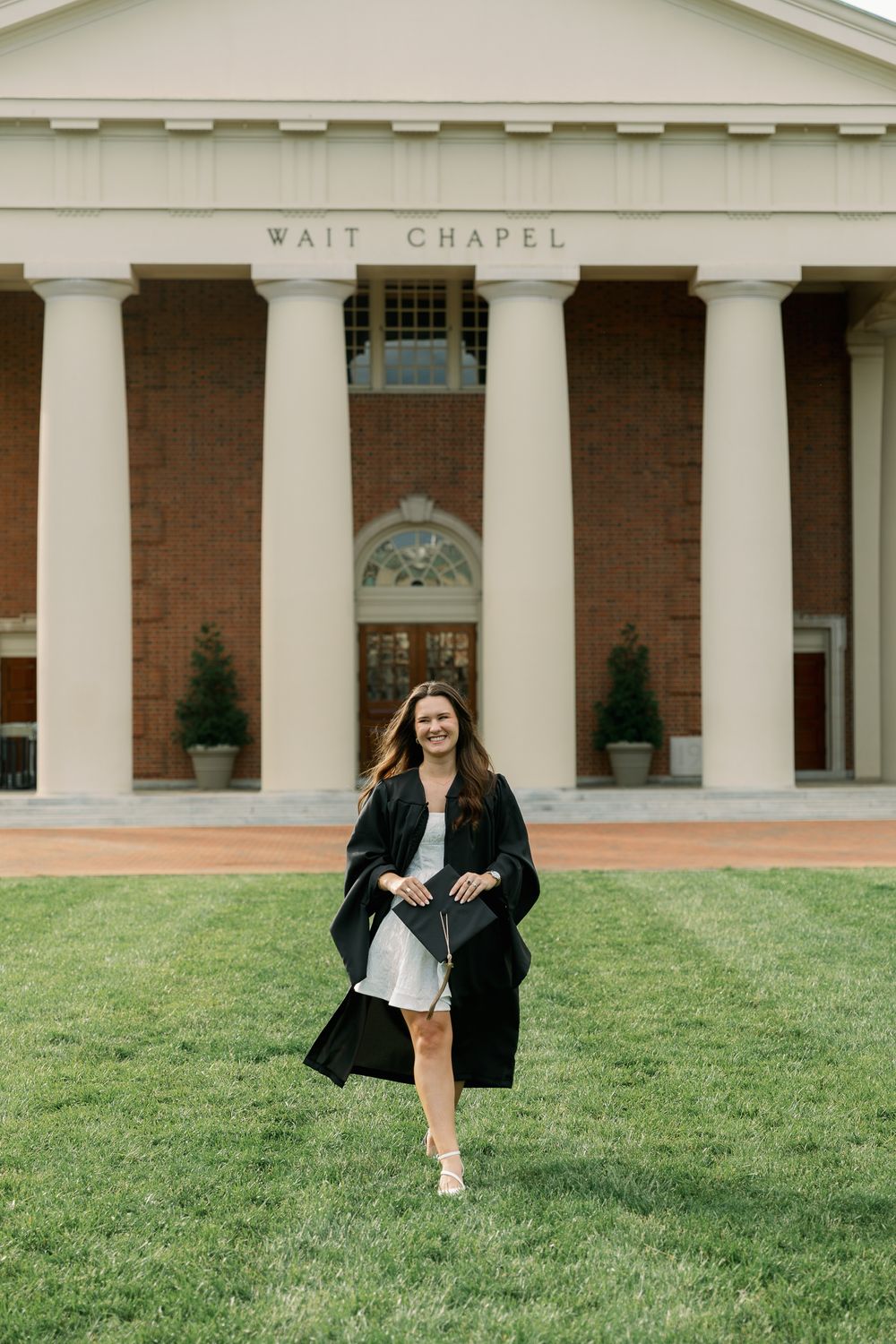 Graduate walks across lawn in front of Wait Chapel's classical columns.