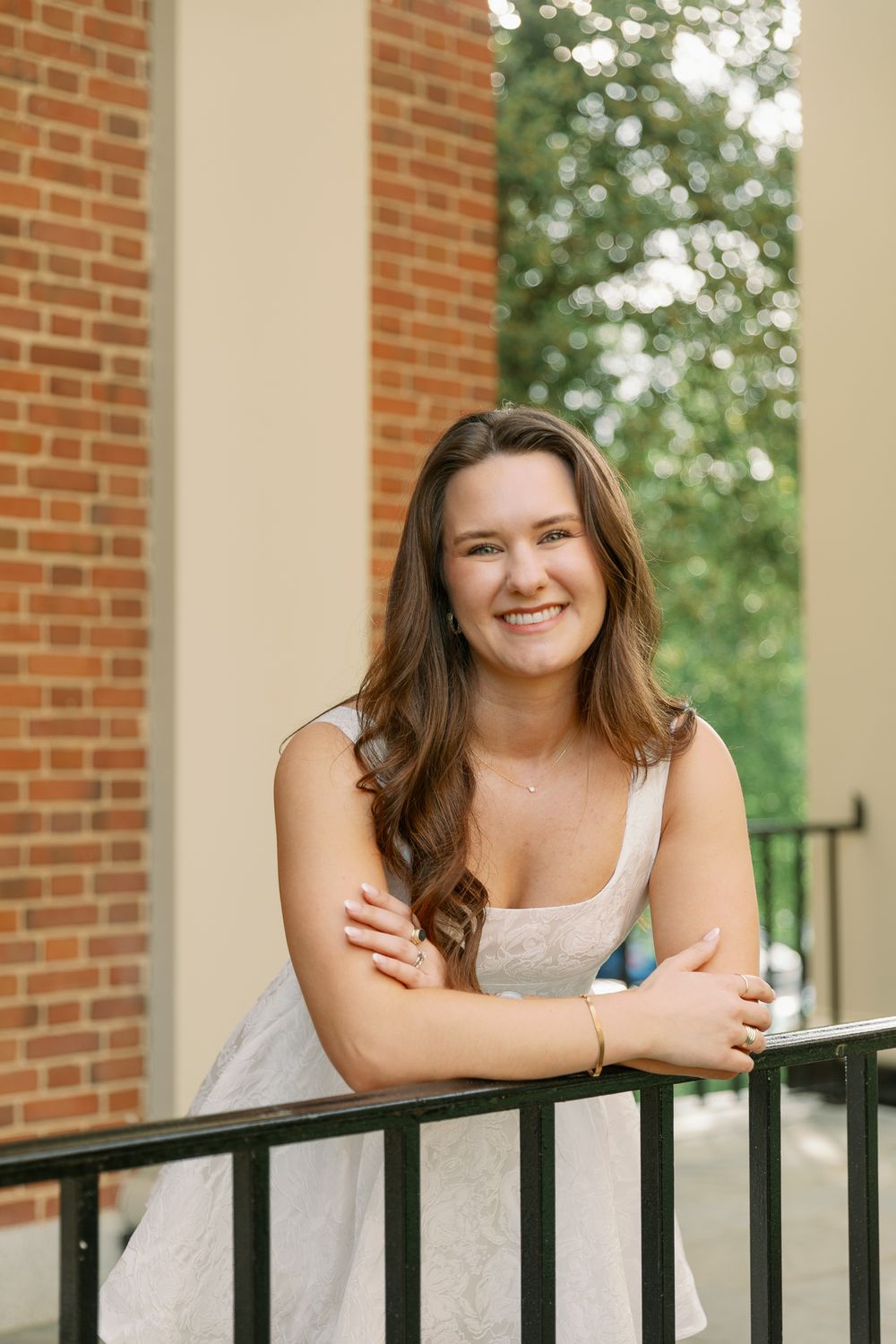 Outdoor portrait session along a black railing with brick and white columns in the background.