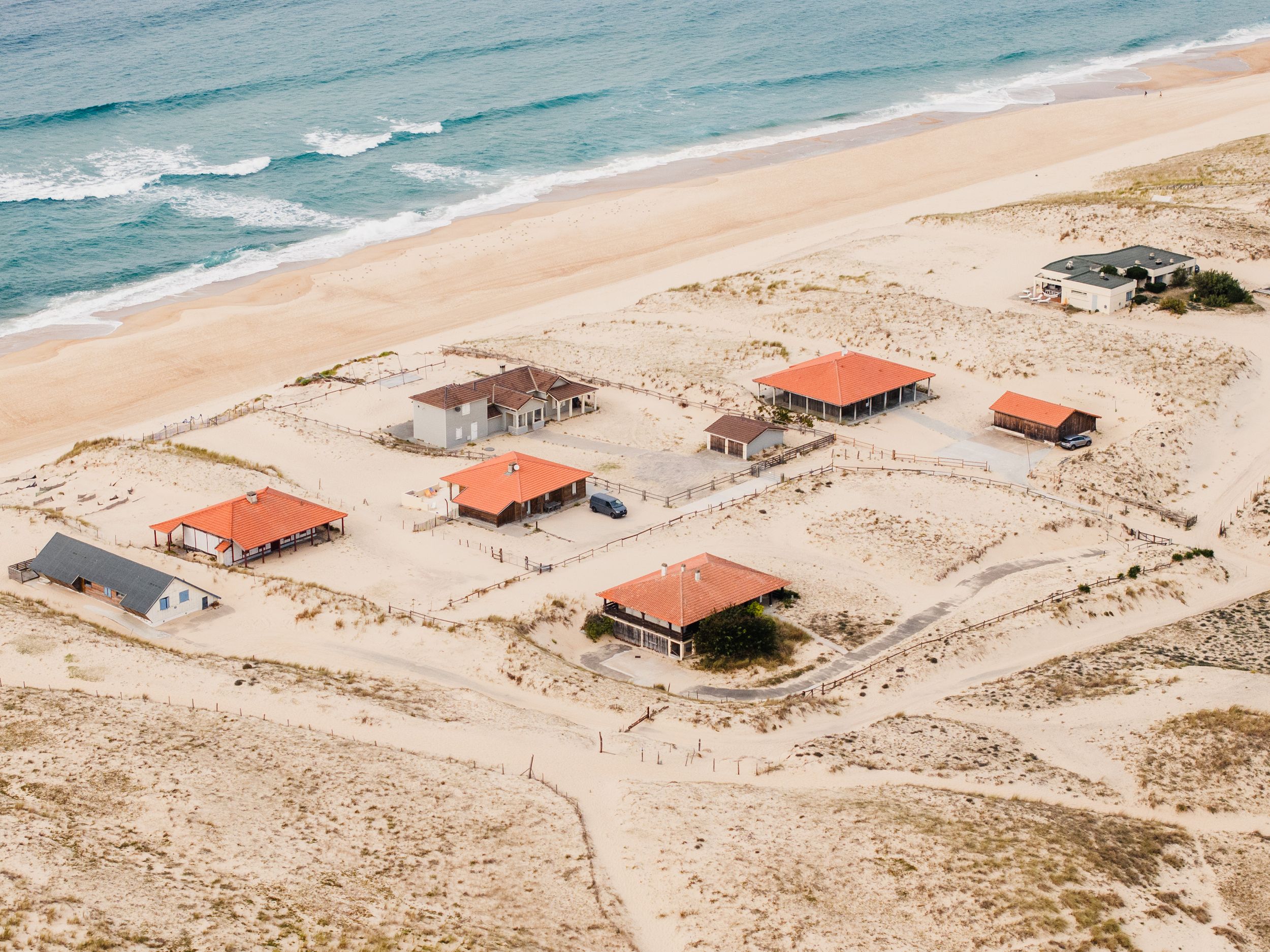 Aerial view of orange-roofed beach houses scattered along a sandy coastal landscape.