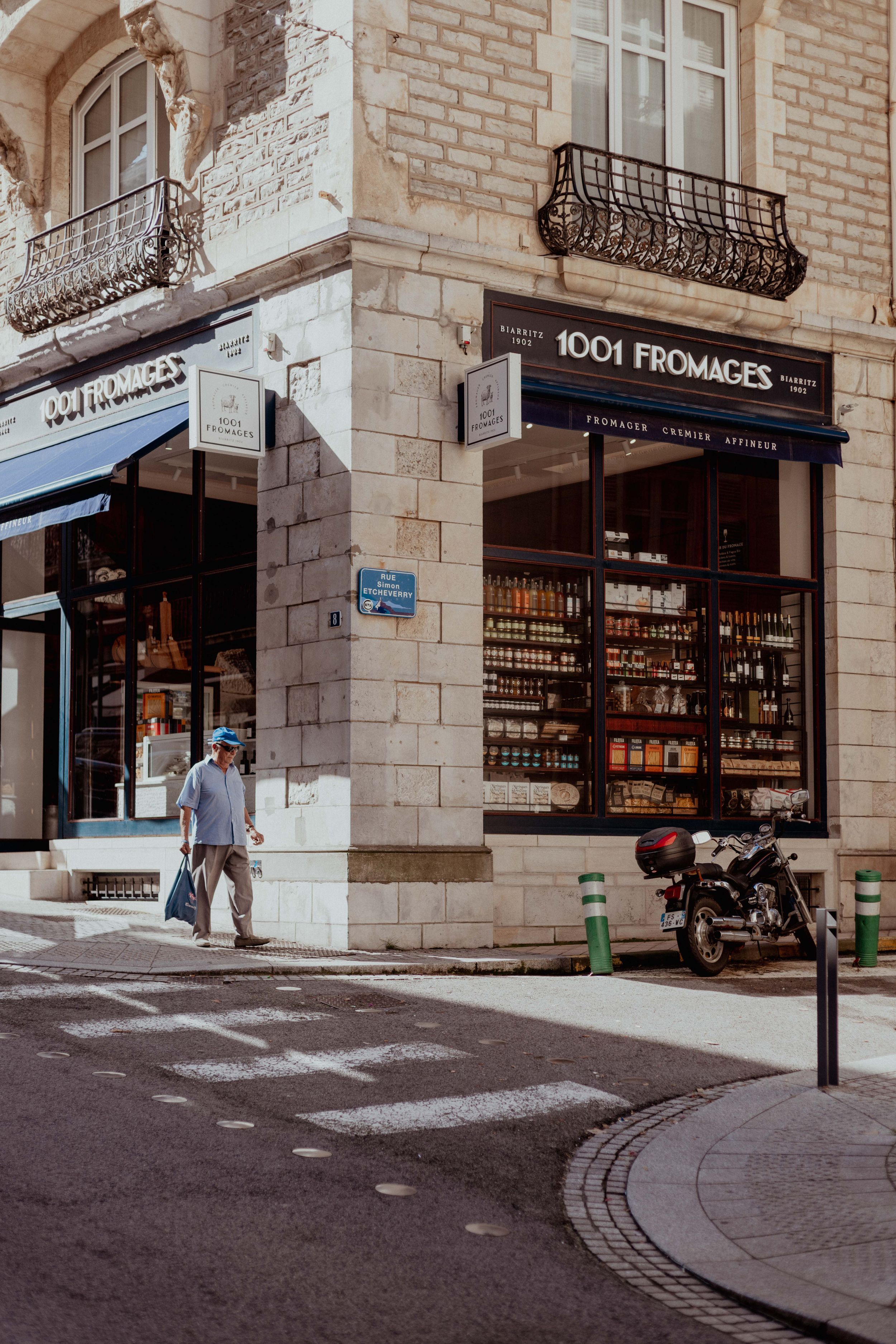 Corner storefront of '1001 Fromages' cheese shop with classic French architecture and motorcycle parked outside.