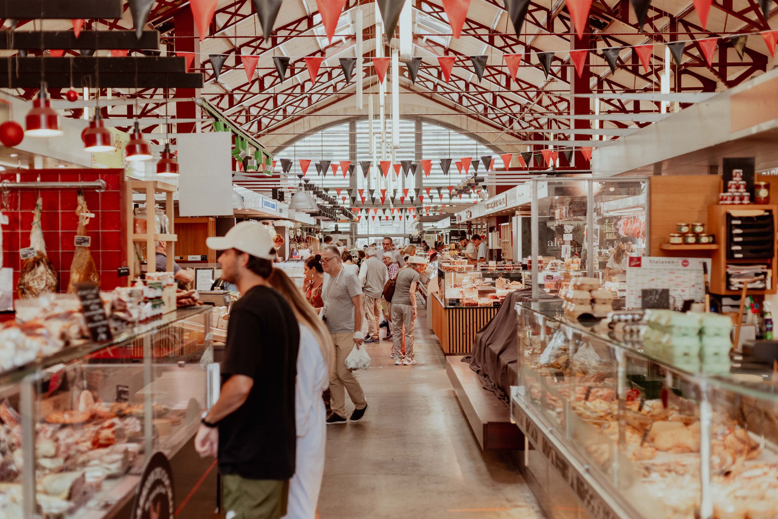 Historic indoor market hall with rows of vendor stalls and decorative red bunting hanging from exposed ceiling beams.