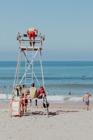 White lifeguard tower on a sunny beach with people climbing and swimming in the ocean.