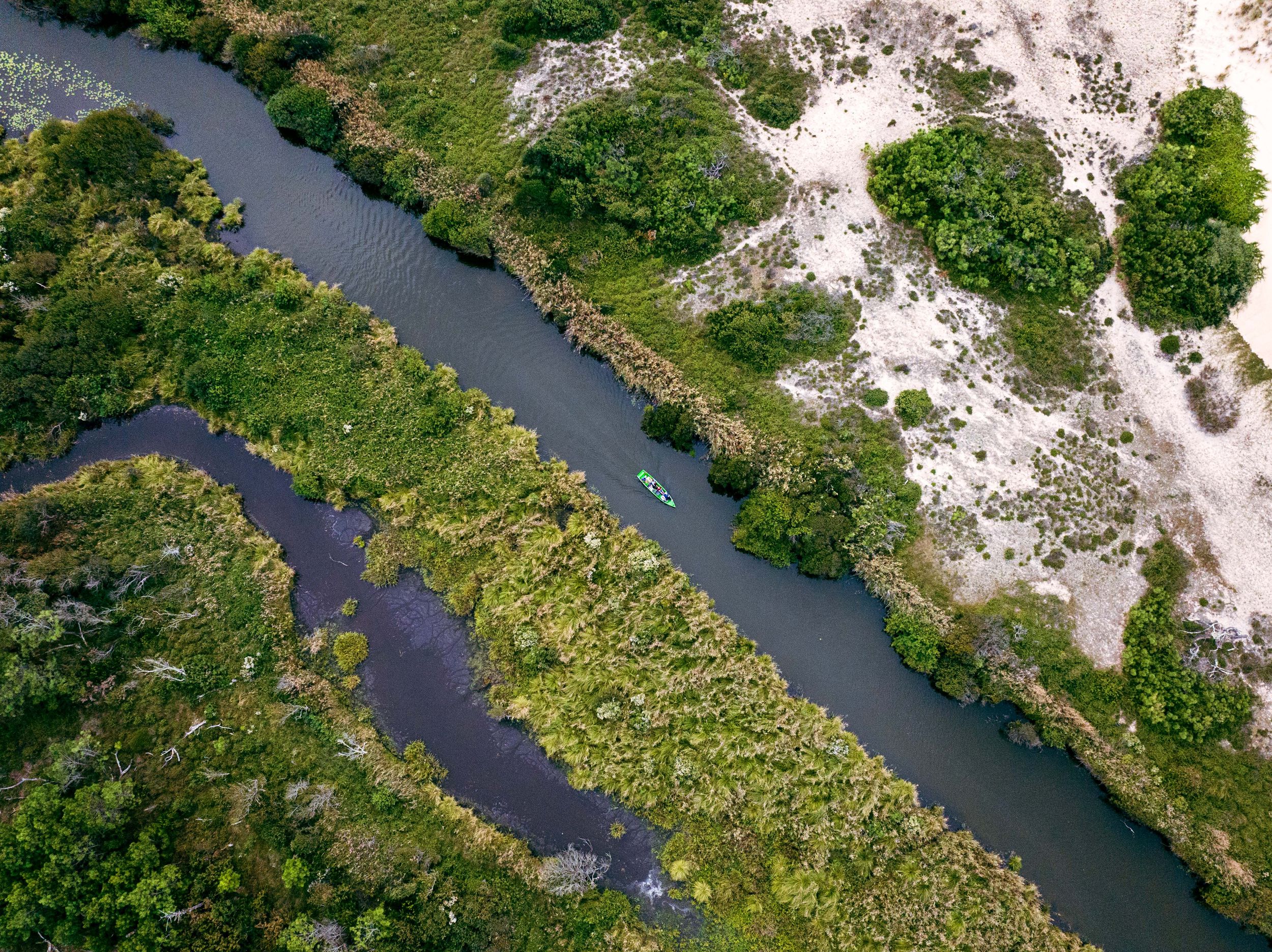 Aerial view of a winding river cutting through lush vegetation and white sandy terrain.