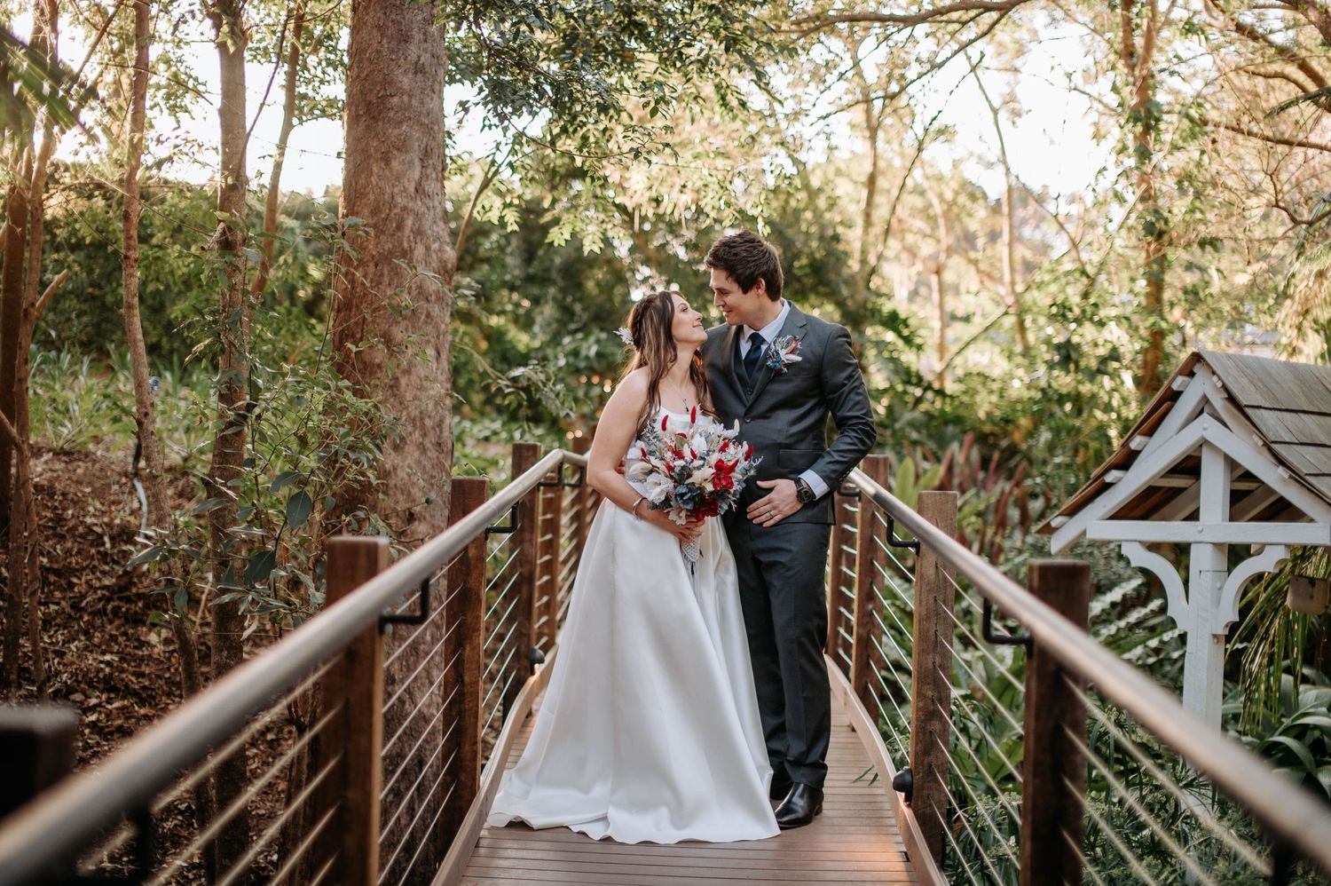 Romantic couple shares a moment on wooden bridge walkway surrounded by trees.