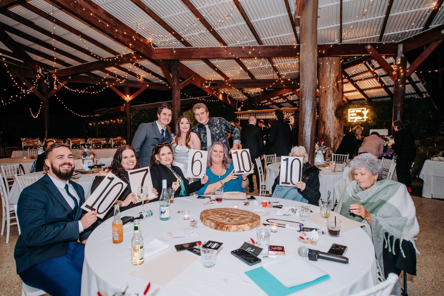 Wedding reception guests enjoying dinner and conversation at decorated round tables under wooden beams.