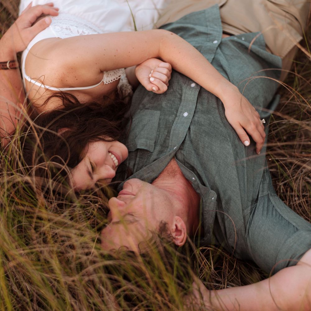 A couple lying together in tall grass during a romantic outdoor photoshoot.