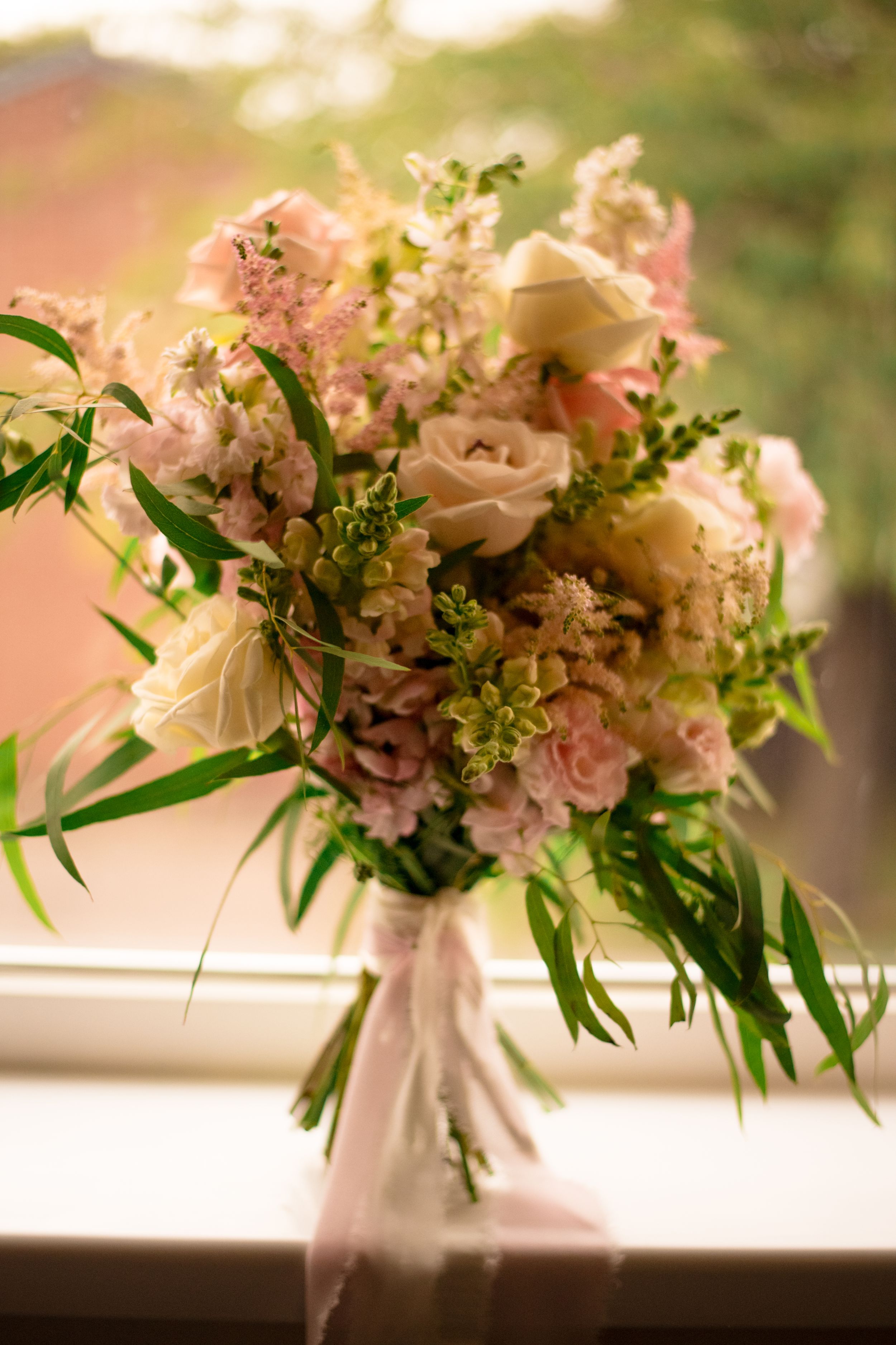 Romantic bridal bouquet with pink and white flowers mixed with greenery by window.