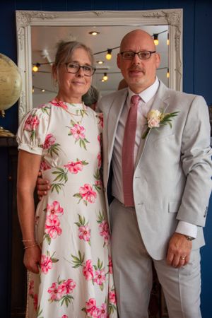 Couple in formal attire poses in front of ornate white framed mirror.
