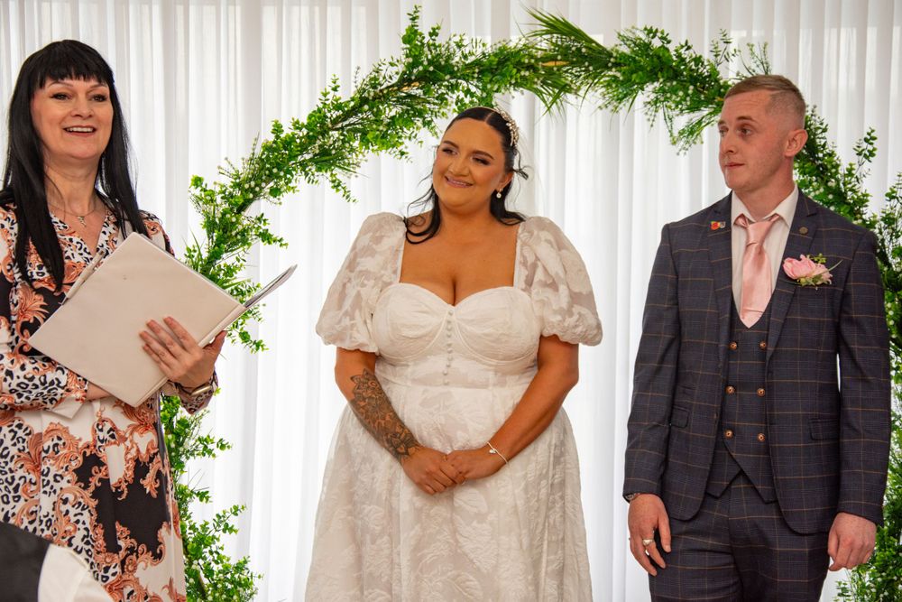Wedding ceremony setup with elegant greenery arch and white backdrop.