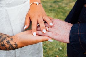 Close-up of tattooed hands exchanging rings during wedding ceremony on grassy background.