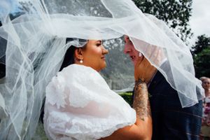 Intimate moment shared under flowing wedding veil during outdoor ceremony.